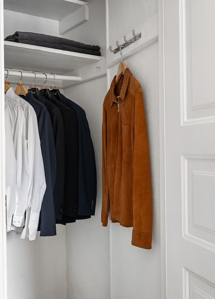 A neatly organised closet with various shirts hanging on a rack and a brown shirt in front.