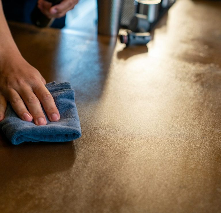 A hand wiping a wooden surface with a blue cloth.