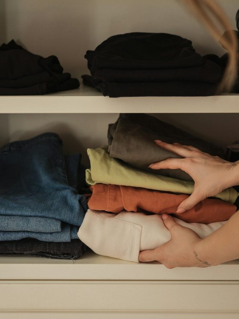 A person arranging neatly folded clothes on a shelf.