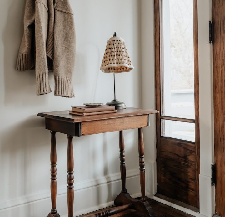 A wooden table with books and a lamp, beside a door and a hanging sweater.